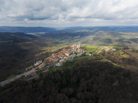 Aerial view of a medieval hilltop town crowned with terracotta roofs and ancient stone walls, basking under a soft, diffused sunlight, Motovun, Istria County, Croatia.