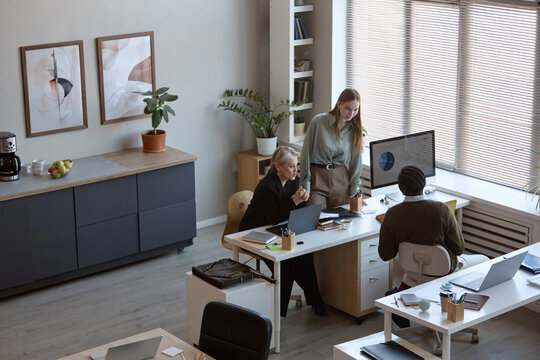 Wide angle shot of diverse business team reviewing analytics on desktop monitor during office meeting. Supporting corporate strategy, teamwork, management training, workplace communication