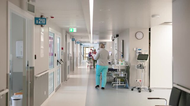 A hospital hallway with medical staff moving a patient on a stretcher, surrounded by clinical equipment and room signage, illustrating active healthcare operations and emergency readiness