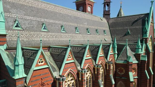 Close aerial orbit reveals intricate rooftop of Oscar Fredriks Kyrka with chevron slate tiles, copper dormer windows, Gothic gabled buttresses and decorative pinnacles against blue sky