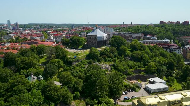Drone approaches Skansen Kronan historic octagonal stone fortress rising above green wooded hilltop with sweeping Gothenburg red-roofed cityscape all around