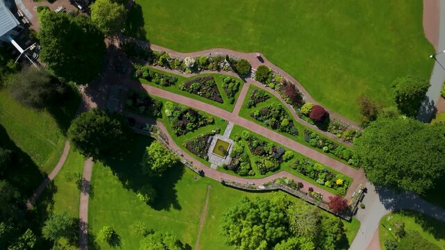 Spinning top-down drone rises above Gothenburg Botanical Garden formal parterre revealing stunning eye-shaped garden layout with cross pathways and central pond from directly overhead