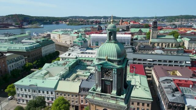Drone orbits tight around Domkyrkan copper-green dome and ornate clock tower revealing Gothenburg harbor river and Karlatornet skyscraper beyond