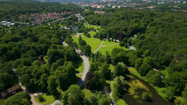 Drone glides forward high above lush Slottsskogen park in Gothenburg revealing vast green canopy, open meadows, winding paths and the city stretching to the horizon