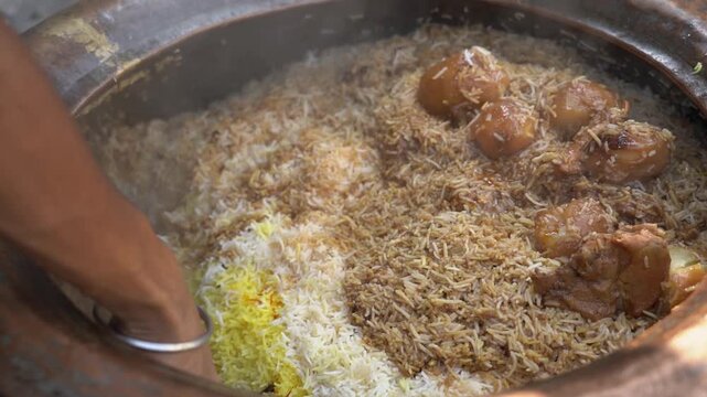 Close up of a street food vendor in India serving fresh, steaming chicken biryani with basmati rice and potatoes from a traditional clay handi.