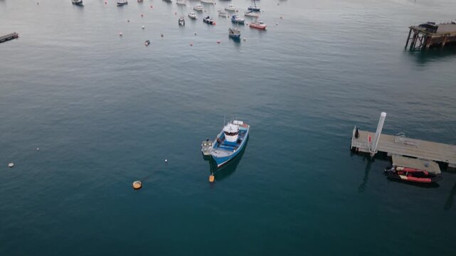 St Peter Port Harbour,Guernsey,droppingl drone footage from views of Herm,Jethou and Sark over swinging moorings ending with overhead shots of boats on moorings on calm day at sunset