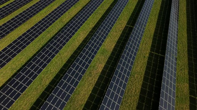 Aerial tilt up of solar panel farm on rural grass field in USA. Sunny day in early spring with traffic on highway in background. Blue sky in america.