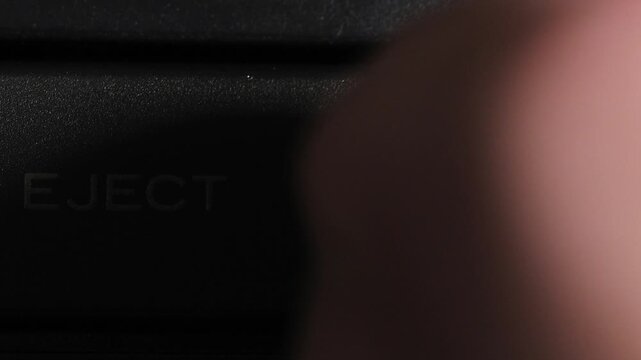 Finger presses blue eject key on right beside gold eject label on left of black camcorder