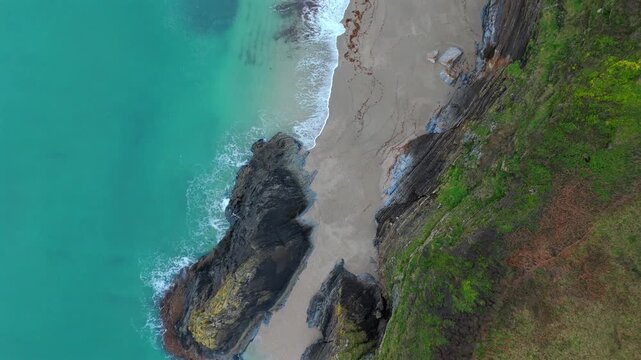 Aerial view of the beach where turquoise water meets the sandy shore, contrasting with the dark rocks and green grass on the cliff, Fowey, Cornwall, United Kingdom.