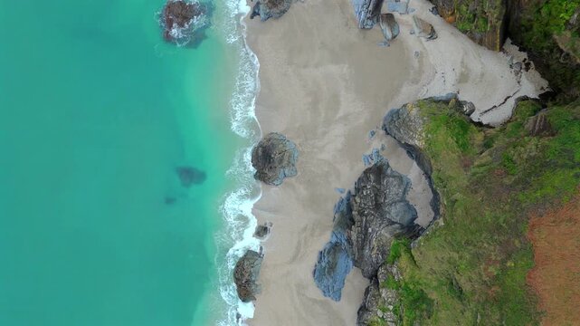 Aerial view of turquoise waters meet a sandy beach, contrasting with the rugged cliffs covered in green vegetation, Fowey, Cornwall, United Kingdom.