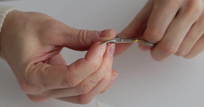 Female hands using nail scissors to remove cuticles during a manicure on a white background