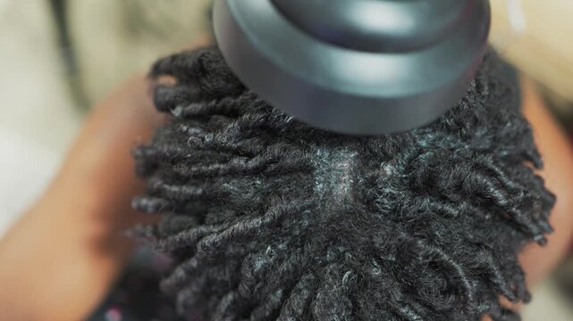 Overhead, macro view of a person with natural Type 4 Afro-textured starter locs during a salon drying session. 