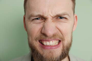 Obraz premium Resentful man on light green background, closeup