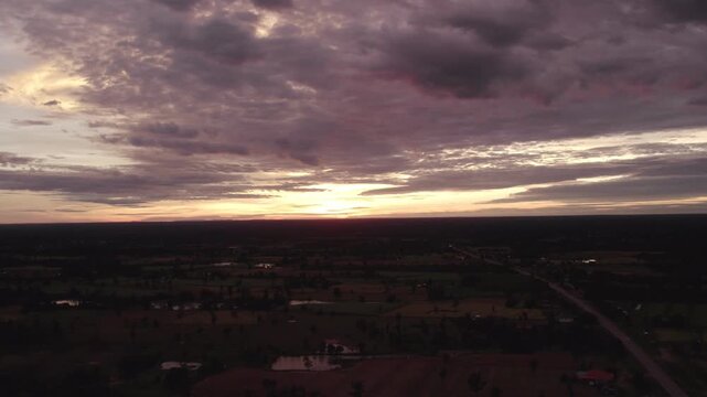 High altitude panning motion flying motion view of the setting sun over rural rtropical landcape, with couldy sky and hazy horizon in the background.