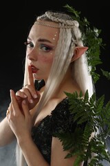 Fototapeta premium Beautiful elf girl with floral decor on black background with smoke