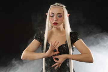 Fototapeta premium Beautiful girl dressed as elf on black background with smoke