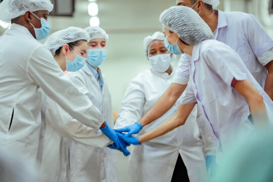 Multicultural factory team puts hands together in teamwork gesture before starting production line. Scene reflects strong collaboration, readiness for work, and positive industrial workplace culture.