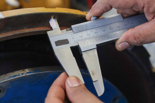 Close up of a mechanic using a steel vernier caliper to measure the internal diameter of a heavy machine component on a yellow industrial engine during a professional maintenance service.