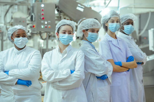 Multicultural factory workers stand in canning production line monitoring equipment and workflow. Concept emphasizes teamwork, hygiene control and efficient food manufacturing standards.