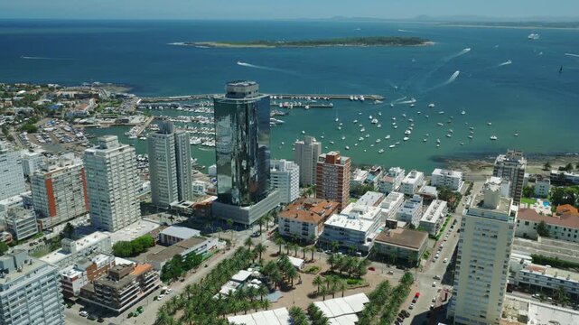 Aerial view of buildings, boats, and Isla de Lobos under a clear sky, creating a stunning contrast between urban and natural elements, Punta del Este, Departamento de Maldonado, Uruguay.