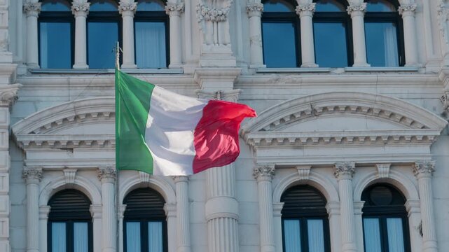 Italian national flag waving in the wind in front of the ornate windows of the Town Hall in Piazza Unita d Italia in Trieste Italy during a clear sunny day outdoor