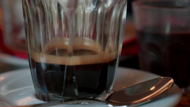 Close up of a typical Trieste coffee called capo in b served in a small glass with saucer and spoon on a table in a historic Italian cafe during a sunny mornings