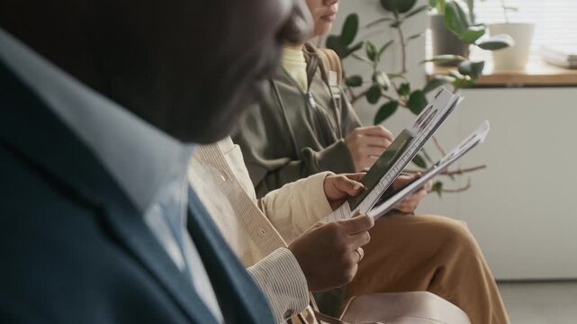 Side medium close-up of multiethnic foreign embassy visitors waiting in queue to apply for business or travel visa, checking documents, passports and photos while chatting