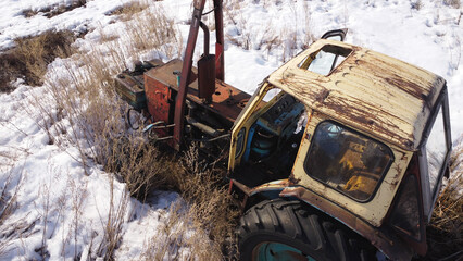 Fototapeta premium shot of a rusty, abandoned tractor sitting in a field of dry, tall grass and patches of snow.