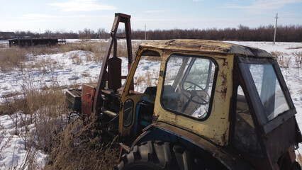 Fototapeta premium shot of a rusty, abandoned tractor sitting in a field of dry, tall grass and patches of snow.