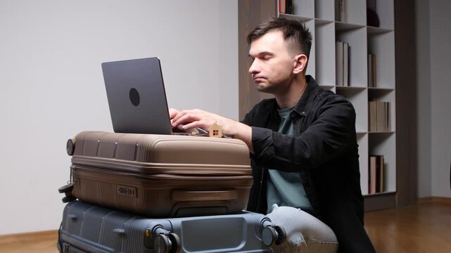 Young man concentrating on his laptop while using stacked suitcases as a makeshift desk, embodying the concept of digital nomadism and remote work during travel or relocation