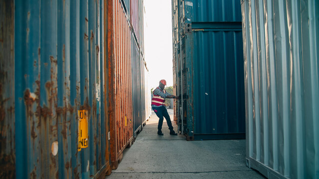 Worker safety vest hard hat shipping container logistics transportation outdoor warehouse manual labor industry worker safety vest and hard hat pushing shipping container door outdoor warehouse