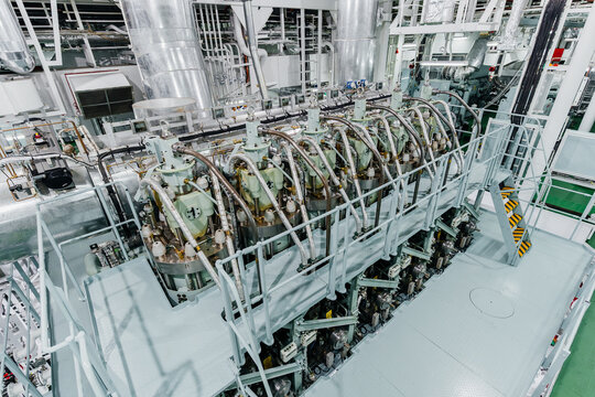 High angle interior view of a massive marine diesel engine inside a ship engine room with complex industrial piping