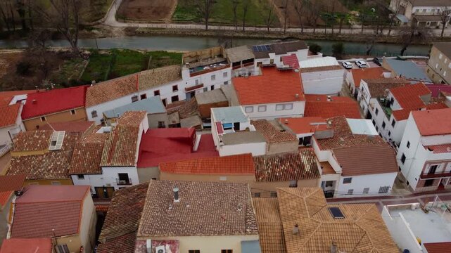 Aerial 4K pedestal shot rising over the terracotta rooftops of a traditional Spanish village. Cinematic reveal of a rural townscape by the J&uacute;car River in Castilla-La Mancha, Spain