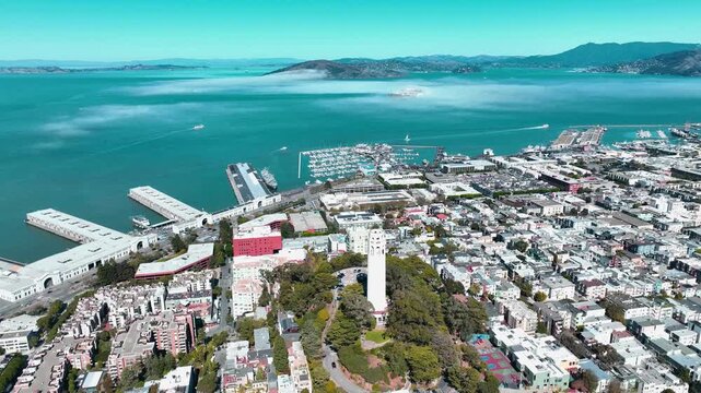 Aerial drone view of Coit Tower and North Beach overlooking San Francisco Bay, with Alcatraz Island, waterfront piers, boats, and low fog on a clear day in San Francisco, California.