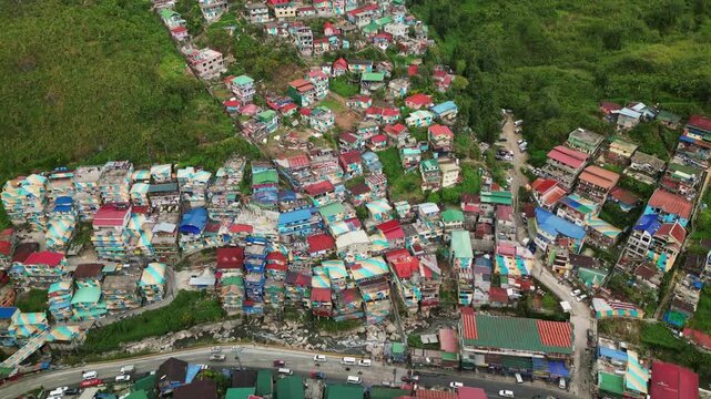 Aerial overview of vibrant, colorful residential house rooftops along hillside community and busy highway - Benguet, Philippines
