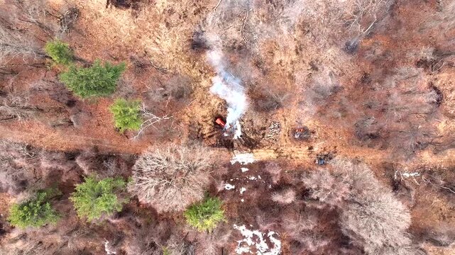 Controlled Burn And Smoke In Dormant Forest Clearing With Tractor At Work On Winter Day. aerial topdown shot