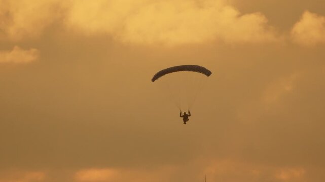 Paraglider sunset adventure featuring a lone silhouetted paraglider floating gracefully through the golden orange evening sky