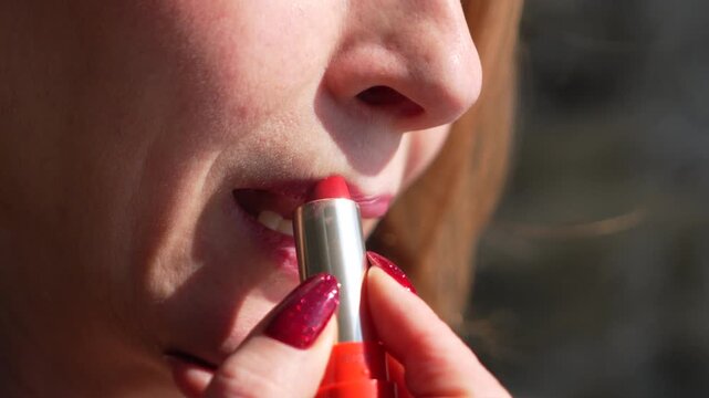 Lipstick makeup woman applying red cosmetic to lips for a glamorous beauty routine outdoors