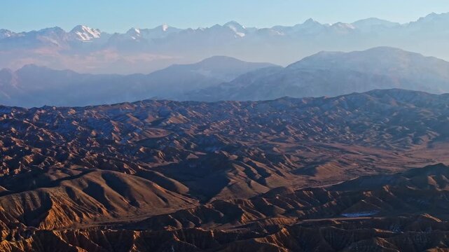 Aerial view captures majestic Ak-Say canyons on south shore of Issyk-Kul lake. Rugged landforms and snow-capped mountains create a serene landscape.