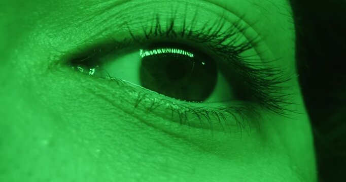 Macro shot up of a brown woman eye in green lighting. Concept of optics and vision, eye health, the beauty and media industries, technical and IT innovations, nightlife themes.