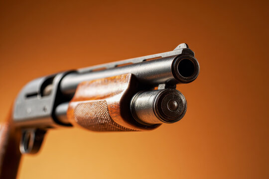 Close-up perspective of a classic pump-action shotgun with wooden grip against a warm brown background highlighting its barrel and mechanical details