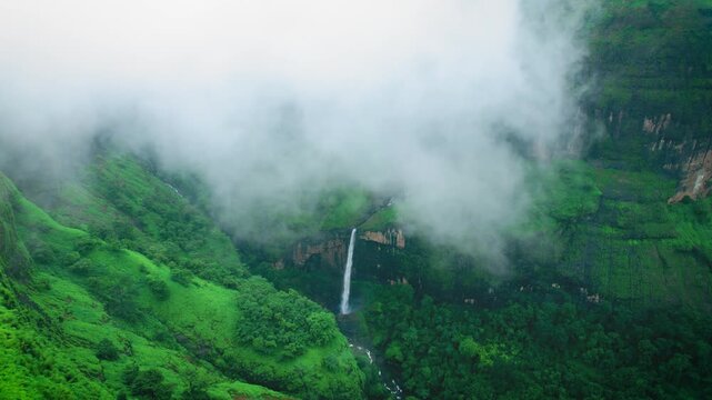 Aerial view of ring waterfall hidden in fog. Beautiful waterfall surrounded by lush green hills and monsoon mist near Tamini Ghat, Maharashtra, India. Clouds covering green valley.

