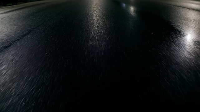 Tracking shot low angle forward movement of wet asphalt road reflecting streetlight glints on quiet urban street at night