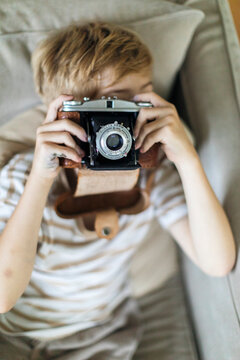 High angle view of boy photographing through vintage camera at home
