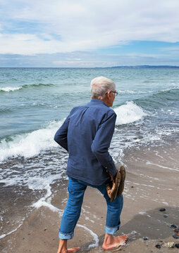 Senior man holding sandals in hand walking on beach against clear sky