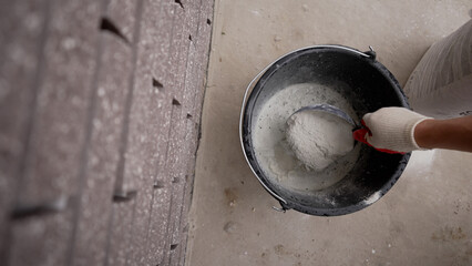 Fototapeta premium Builder's hand in a glove mixing cement or plaster powder in a bucket on a construction site, top view.