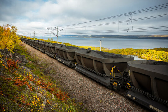 View of rail cars loaded with coal stationed on tracks near river against sky