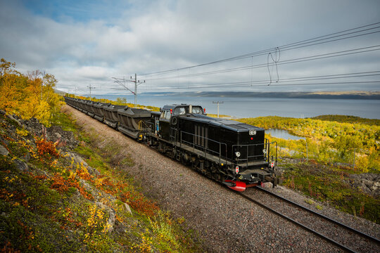 Loaded coal train moving on tracks near sea against sky