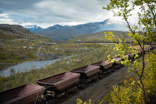 Train with empty coal containers stationed on tracks against scenic mountains
