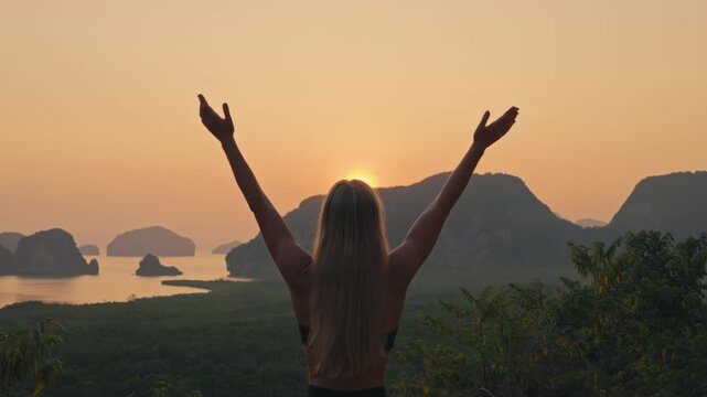 Medium shot upper body from a toned fit woman performing upward salute prayer yoga pose at viewpoint over bay with islands with golden sky
